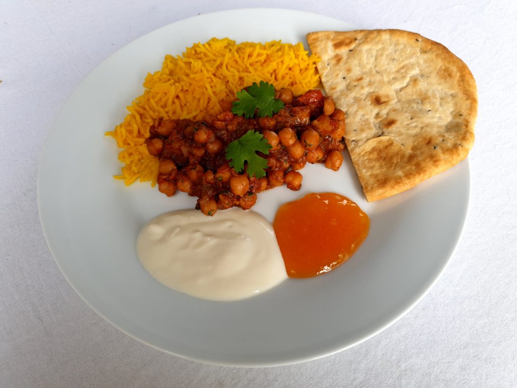 Et bord med hvit duk har en tallerken med chana masala, sammen med gul ris, soyayoghurt, mangochutney og naan. Foto: Elin Bekkebråten Sjølie © 2021
